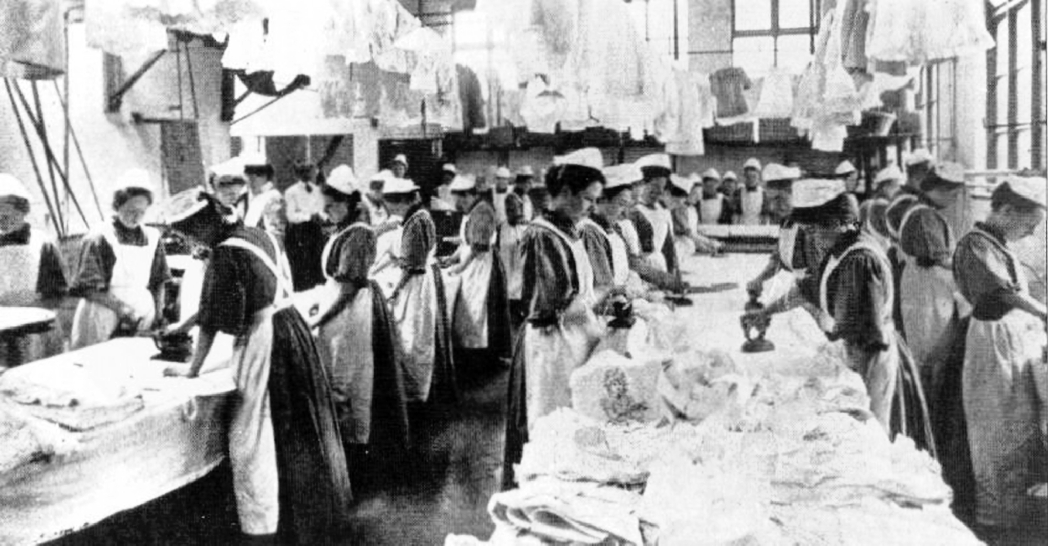 Black-and-white photograph of young women dressed in aprons. They are working in a laundry.