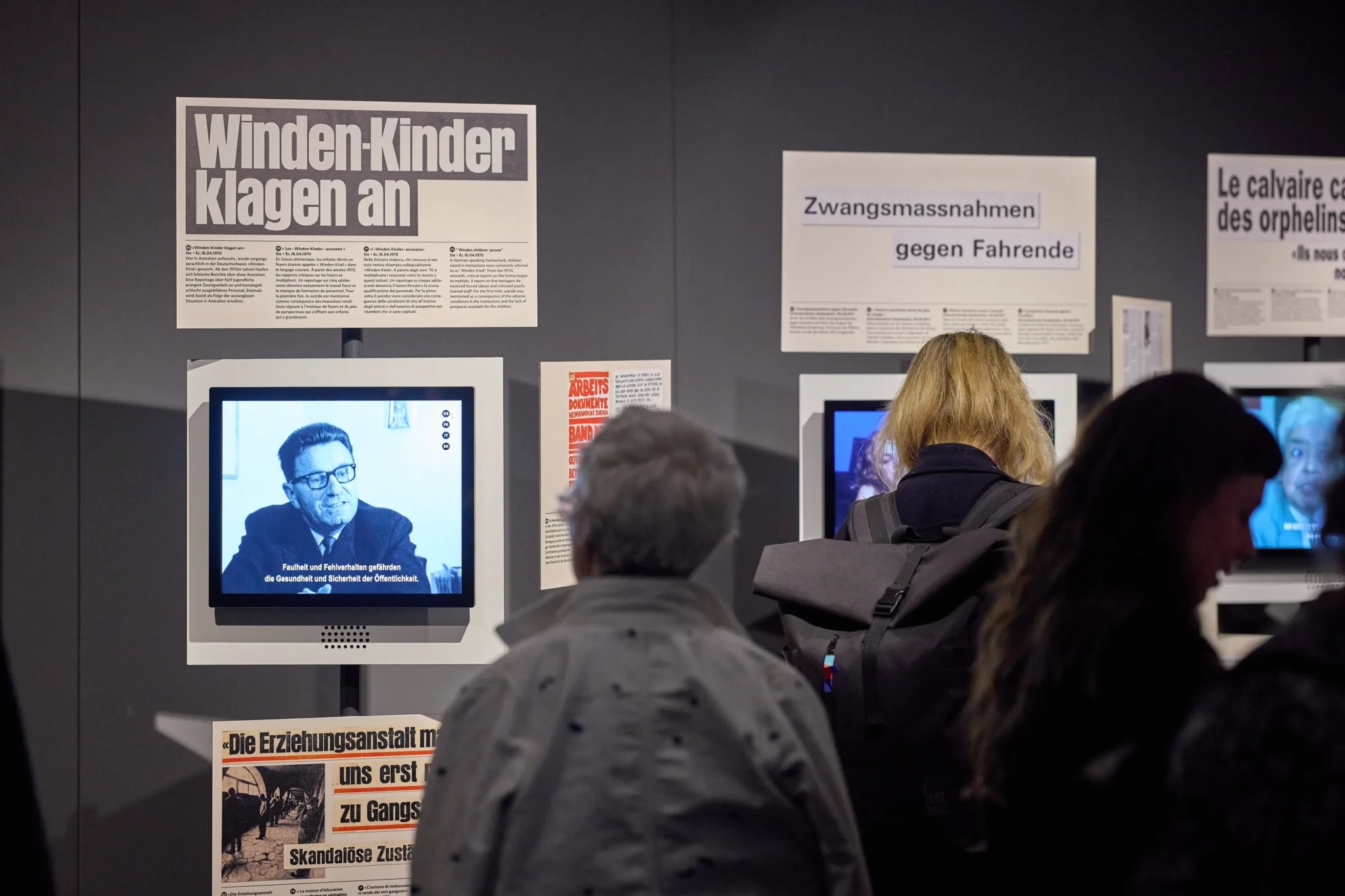 Zwei Personen lesen Zeitungsartikel an einer Plakatwand in der Ausstellung.