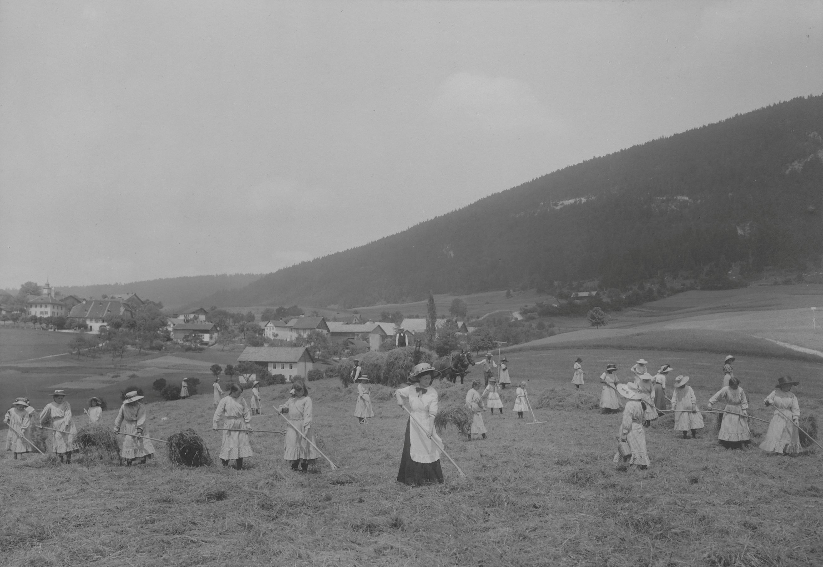 Black-and-white photograph of young women in Sunday clothes working in the fields at the Loveresse reform school. The image is taken from volume 2 of the photo albums of the Bern Canton Welfare Authority and was exhibited at the 1914 National Exhibition in Bern.
