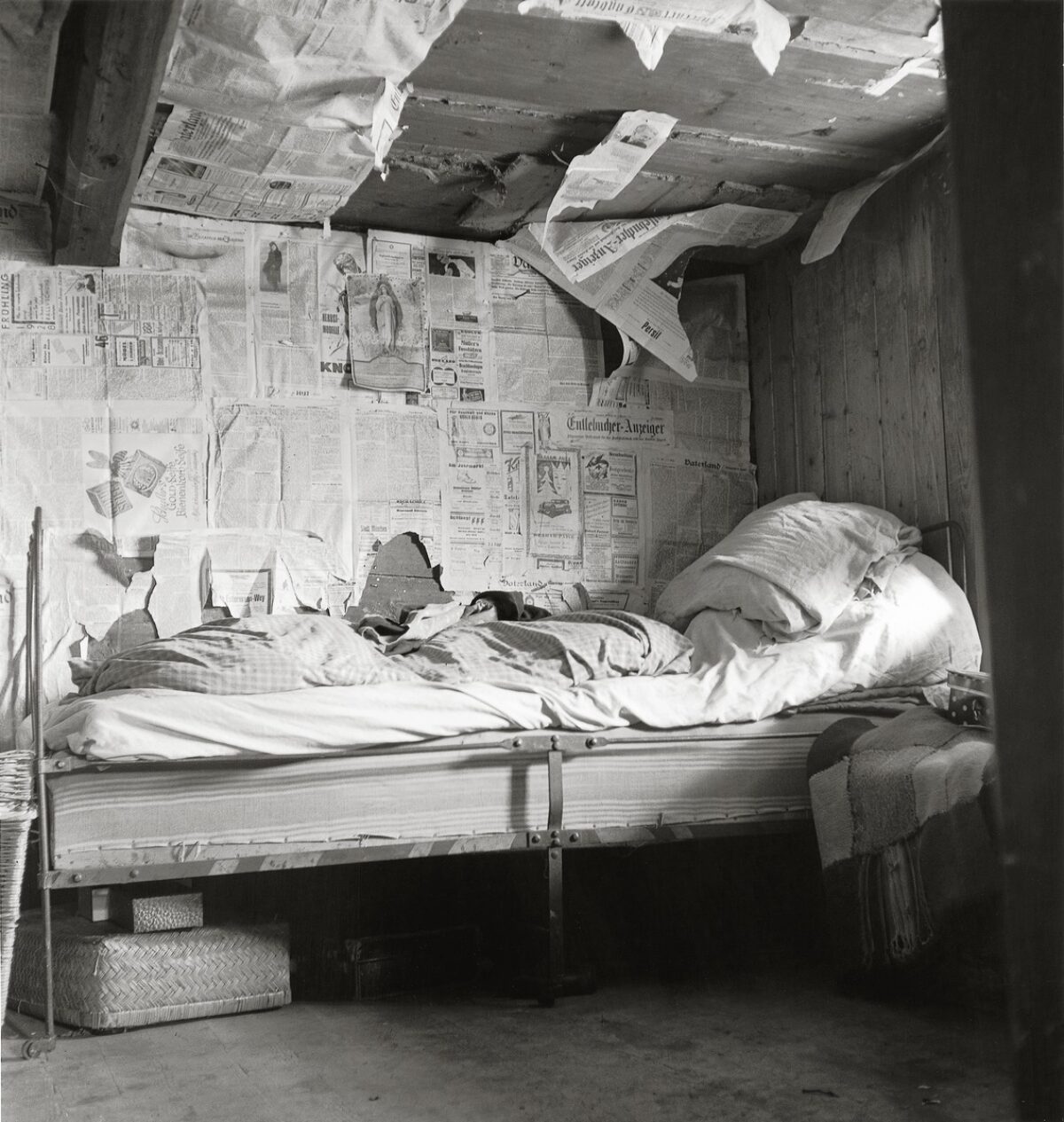 Black-and-white photograph. Bed in a room insulated with old newspapers. The image depicts impoverished living conditions in Flühli in Entlebuch, 1947.