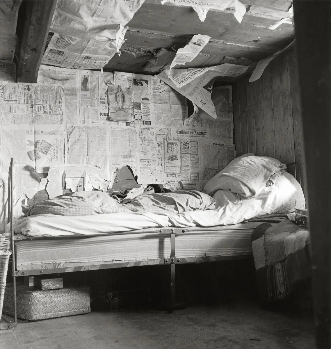 Black-and-white photograph. Bed in a room insulated with old newspapers. The image depicts impoverished living conditions in Flühli in Entlebuch (LU), 1947.